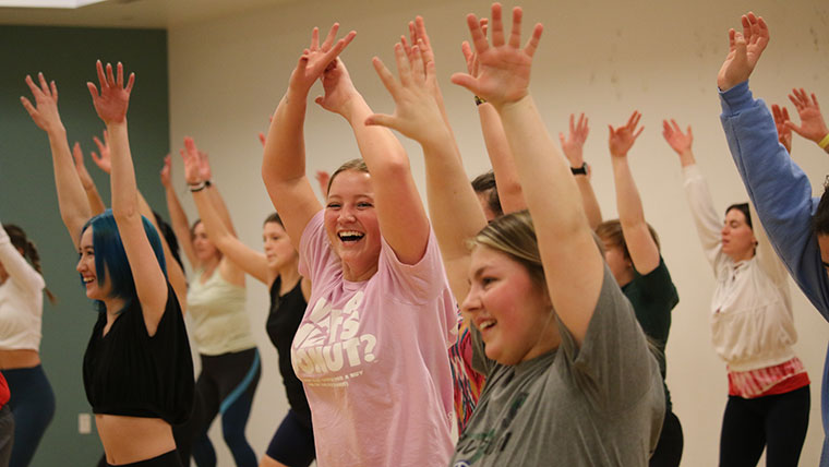 Students participating in a workout class raise their arms joyously.