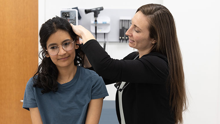 A student try to sit still as a medical professional uses an otoscope to look in her ear.